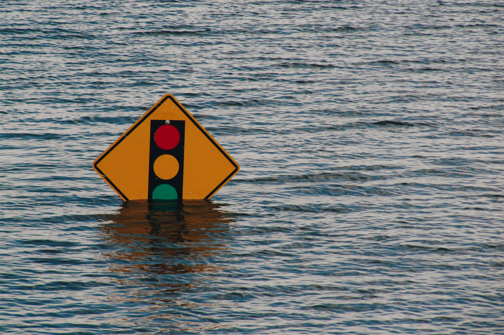 Straßenschild mit Ampel steht unter Wasser. Foto: Kelly Sikkema / Unsplash