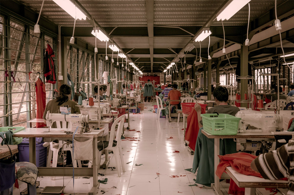 Personen an Nähmaschinen in einer Fabrikhalle.